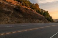 a woman is riding her bicycle down the road with the sunset behind her and hills