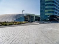 the woman is riding her bike near the building and her reflection on the mirroring glass of the side