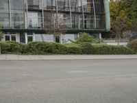 a woman riding on the back of a red bike next to a building and hedges