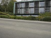 a woman riding on the back of a red bike next to a building and hedges