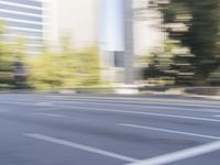 a woman rides a motorcycle in a motion on the side of the street with tall buildings