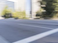 a woman rides a motorcycle in a motion on the side of the street with tall buildings