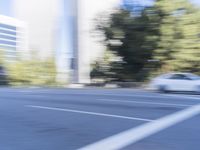 a woman rides a motorcycle in a motion on the side of the street with tall buildings