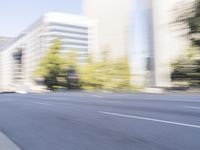 a woman rides a motorcycle in a motion on the side of the street with tall buildings