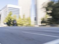 a woman rides a motorcycle in a motion on the side of the street with tall buildings