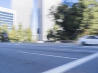 a woman rides a motorcycle in a motion on the side of the street with tall buildings