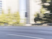 a woman rides a motorcycle in a motion on the side of the street with tall buildings