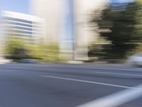 a woman rides a motorcycle in a motion on the side of the street with tall buildings