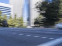 a woman rides a motorcycle in a motion on the side of the street with tall buildings