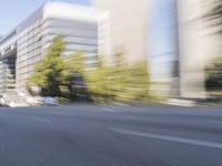 a woman rides a motorcycle in a motion on the side of the street with tall buildings