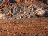 a woman standing in a field next to rocks and animals on a dirt road surrounded by rocky areas