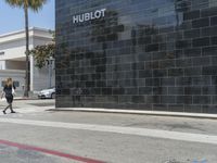 there is a woman walking on the sidewalk near the hublot building in the city