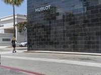 there is a woman walking on the sidewalk near the hublot building in the city