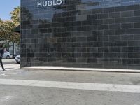 there is a woman walking on the sidewalk near the hublot building in the city