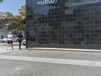 there is a woman walking on the sidewalk near the hublot building in the city