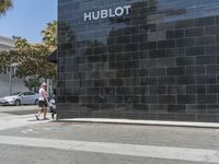 there is a woman walking on the sidewalk near the hublot building in the city