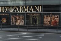 a woman in grey dress walking down street by a storefront of armanit