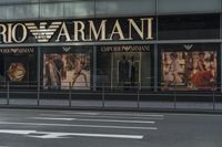 a woman in grey dress walking down street by a storefront of armanit