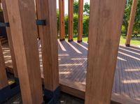 large wooden structures with black posts on wooden decking area with green lawn in background