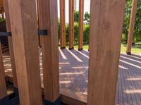 large wooden structures with black posts on wooden decking area with green lawn in background