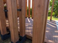 large wooden structures with black posts on wooden decking area with green lawn in background