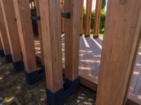 large wooden structures with black posts on wooden decking area with green lawn in background