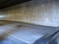 a skateboarder is riding under a large bridge by himself in a parking garage