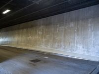 a skateboarder is riding under a large bridge by himself in a parking garage