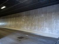 a skateboarder is riding under a large bridge by himself in a parking garage