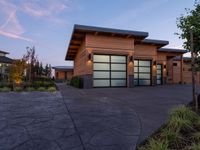 a home with stone driveway and modern garages at sunset with sky in the background