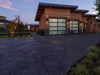 a home with stone driveway and modern garages at sunset with sky in the background