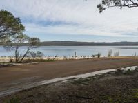 a sandy road next to a lake with no traffic on it and lots of water