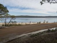 a sandy road next to a lake with no traffic on it and lots of water