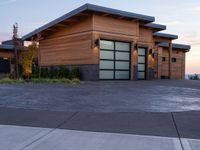 this house has wood clad walls and garage doors along with large windows, and a driveway leading to the front of the house