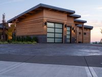 this house has wood clad walls and garage doors along with large windows, and a driveway leading to the front of the house