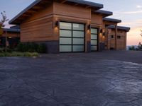 this house has wood clad walls and garage doors along with large windows, and a driveway leading to the front of the house