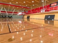 a wooden basketball court surrounded by glass walls and beams with red walls above a red wall