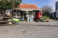 the wooden benches are sitting at the stand with the plants outside of the store in the sunshine