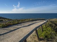 a long, narrow wooden boardwalk on the shore near the ocean in front of a grassy field