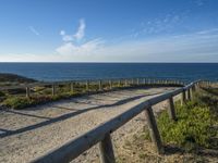 a long, narrow wooden boardwalk on the shore near the ocean in front of a grassy field