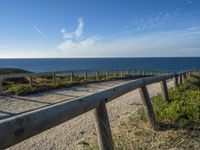 a long, narrow wooden boardwalk on the shore near the ocean in front of a grassy field