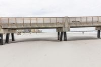 a wooden bridge across the beach, leading to a sandy area with tall sand dunes