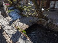 there is a little wooden bridge that is over a stream of water to go under a building