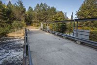 a wooden bridge spans across the forest from a water fall spill, along with a dam