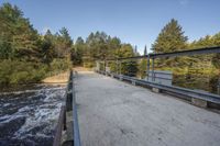 a wooden bridge spans across the forest from a water fall spill, along with a dam