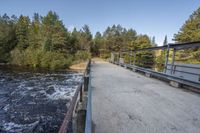 a wooden bridge spans across the forest from a water fall spill, along with a dam