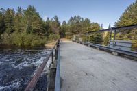 a wooden bridge spans across the forest from a water fall spill, along with a dam