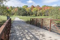 a wooden bridge over a paved path in the autumntime with fall foliage and a path winding through it