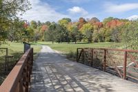 a wooden bridge over a paved path in the autumntime with fall foliage and a path winding through it