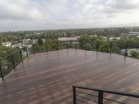 a wooden deck overlooking the city and some trees with an iron rail on it is being used as a railing